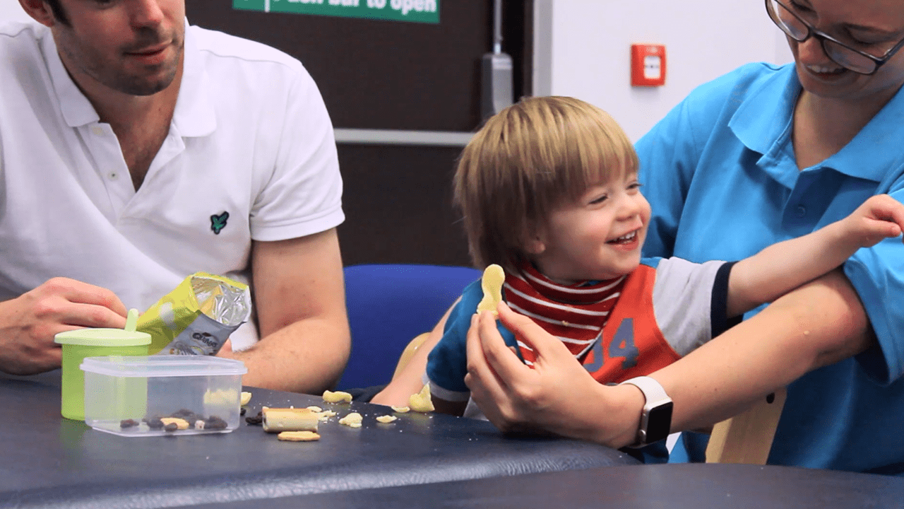 Alistair laughing and smiling with parents and therapists