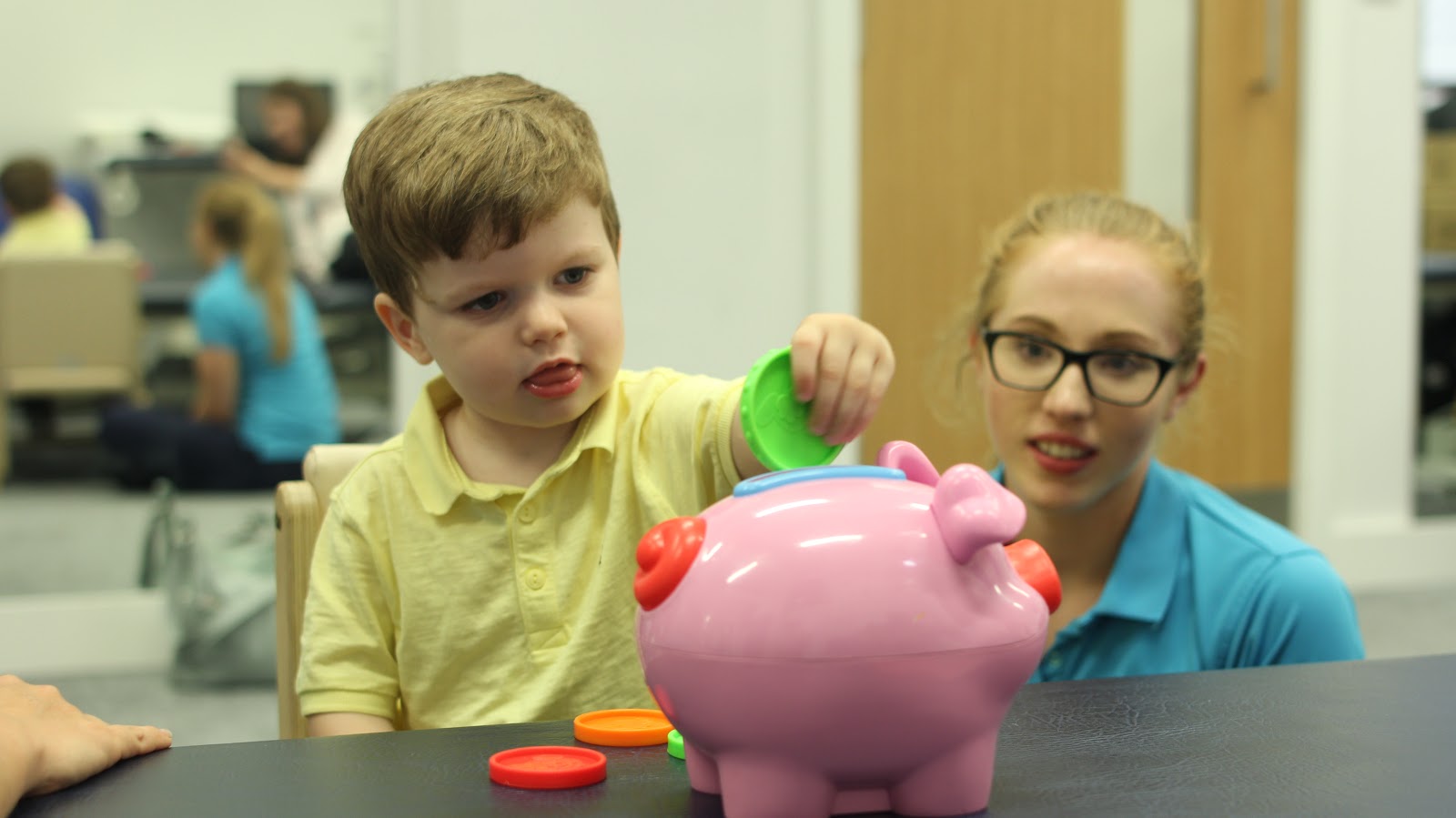 Finlay using pincer grip to grab coins and place them into a money bank