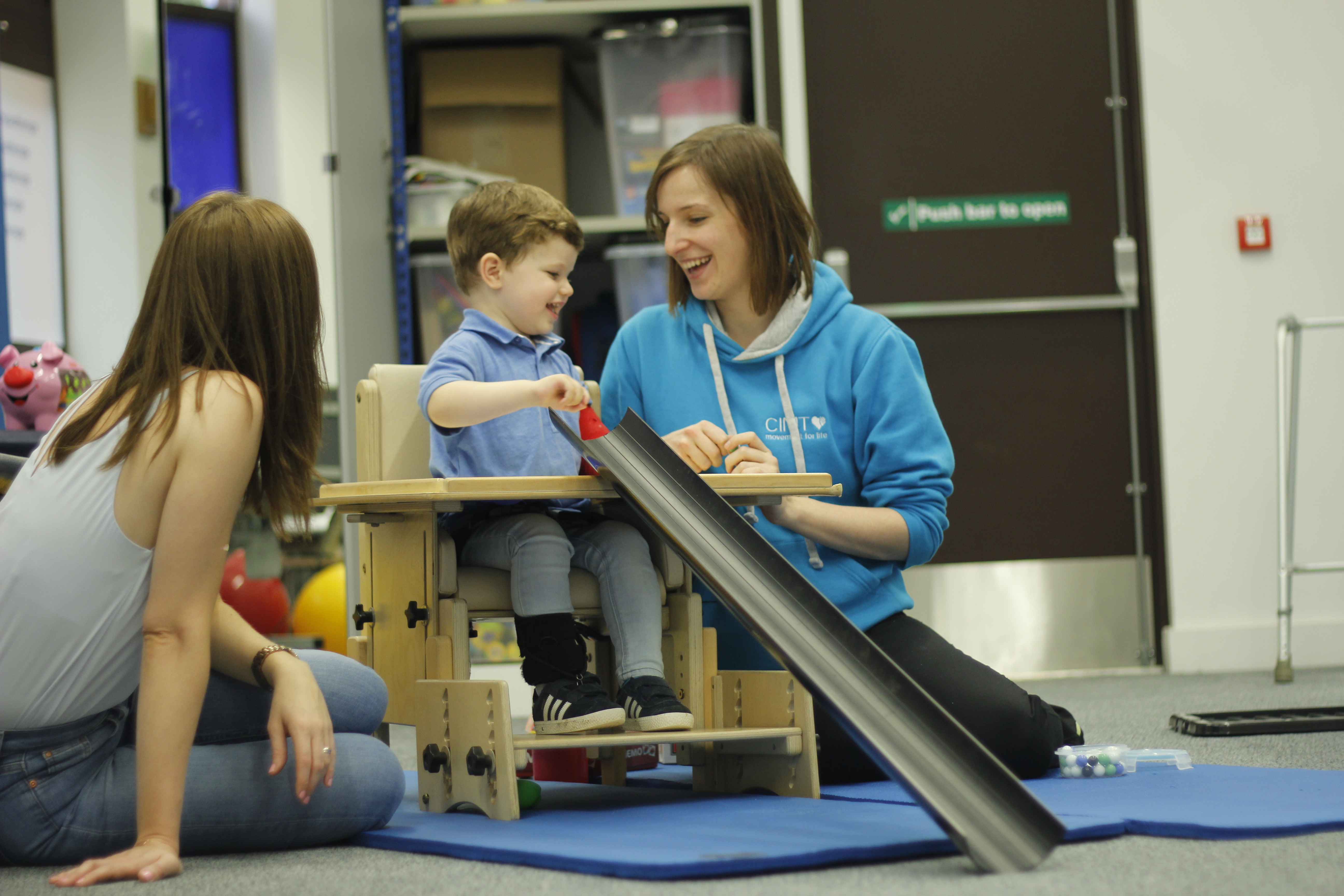 Finlay rolling a ball down a tube with support from therapist.