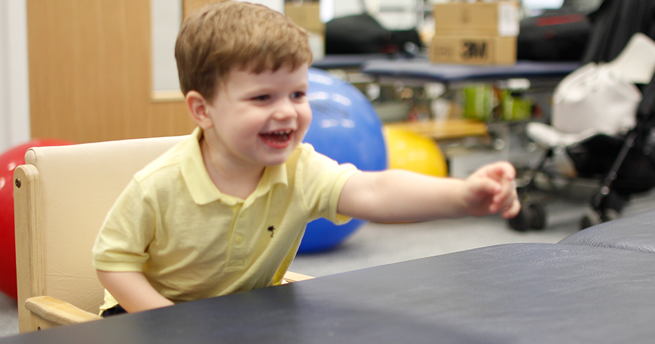 Finlay reaching out to grab object from therapist.