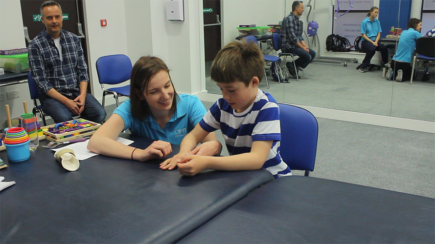 Harvey moving fingers on weaker arm with help from CIMT therapist.