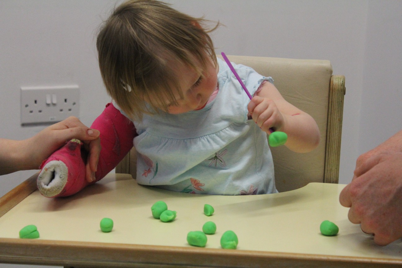 Leah putting objects into money bank using weaker arm.