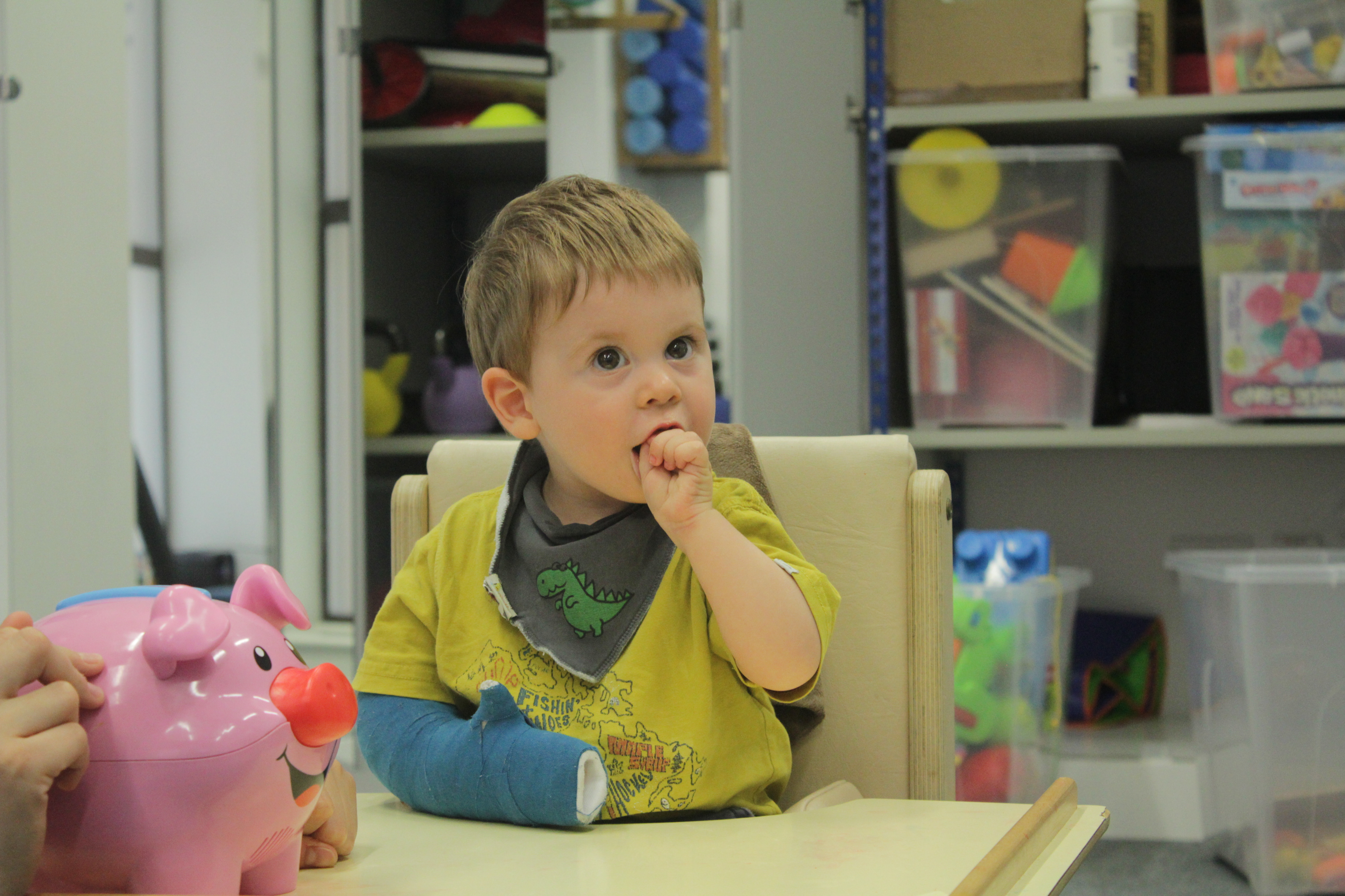 Thomas putting objects into money bank using weaker arm.